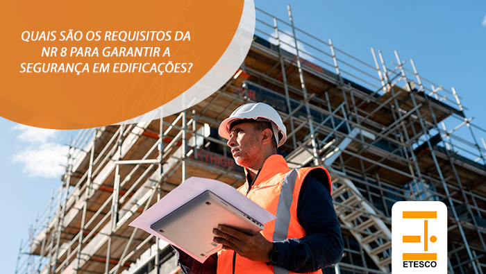 Engenheiro com colete e capacete analisa prancheta em obra com andaimes ao fundo, representando segurança em edificações conforme a NR 8.